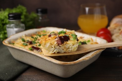 Photo of Taking piece of tasty sausage casserole from baking dish at table, closeup