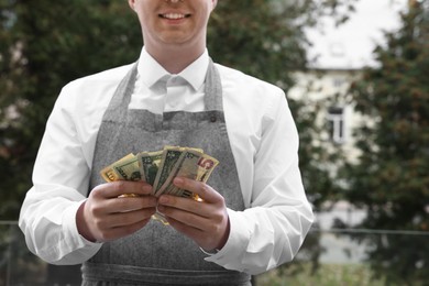 Photo of Happy waiter holding tips in outdoor cafe, closeup