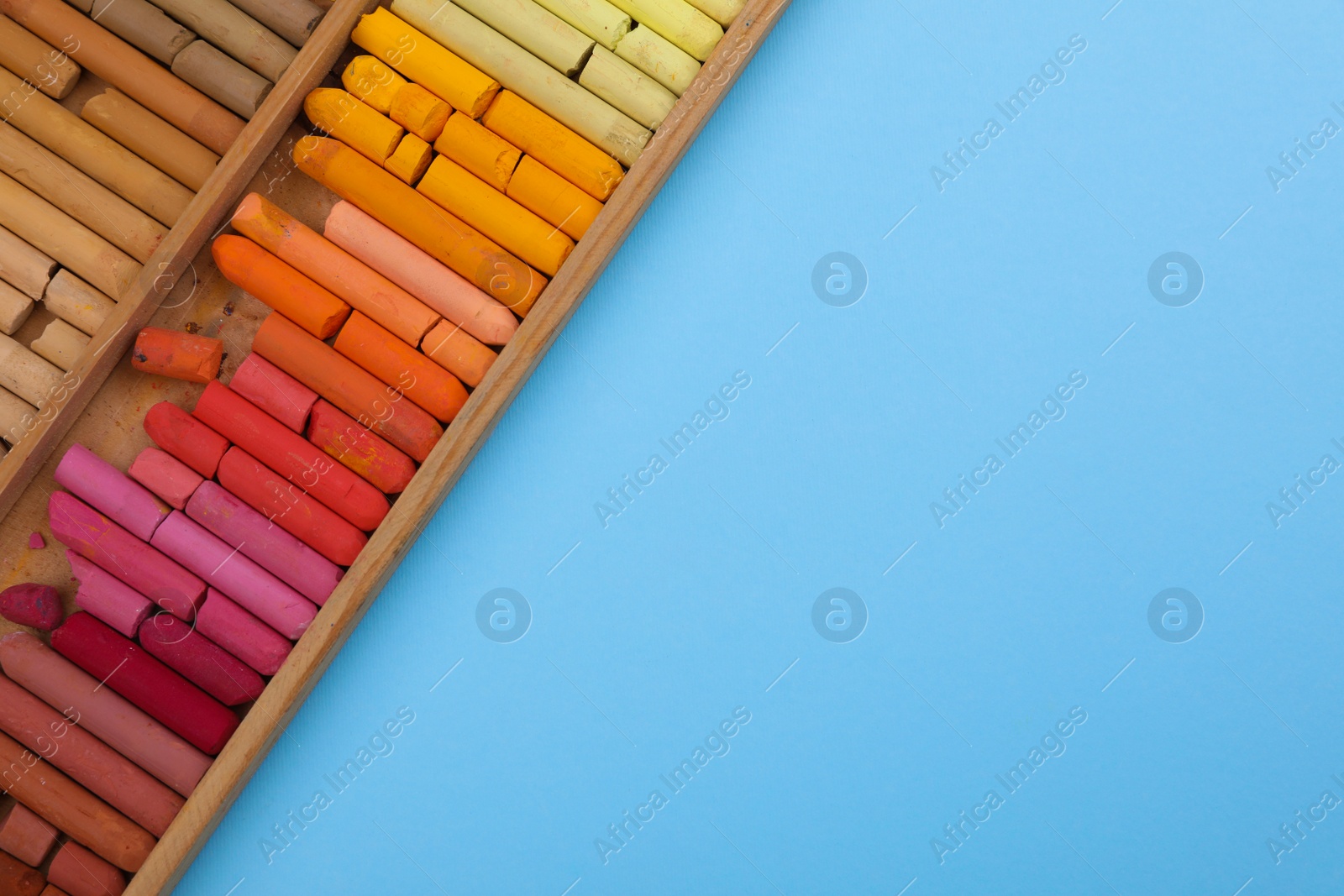 Photo of Set of soft pastels in wooden box on light blue background, top view with space for text. Drawing material