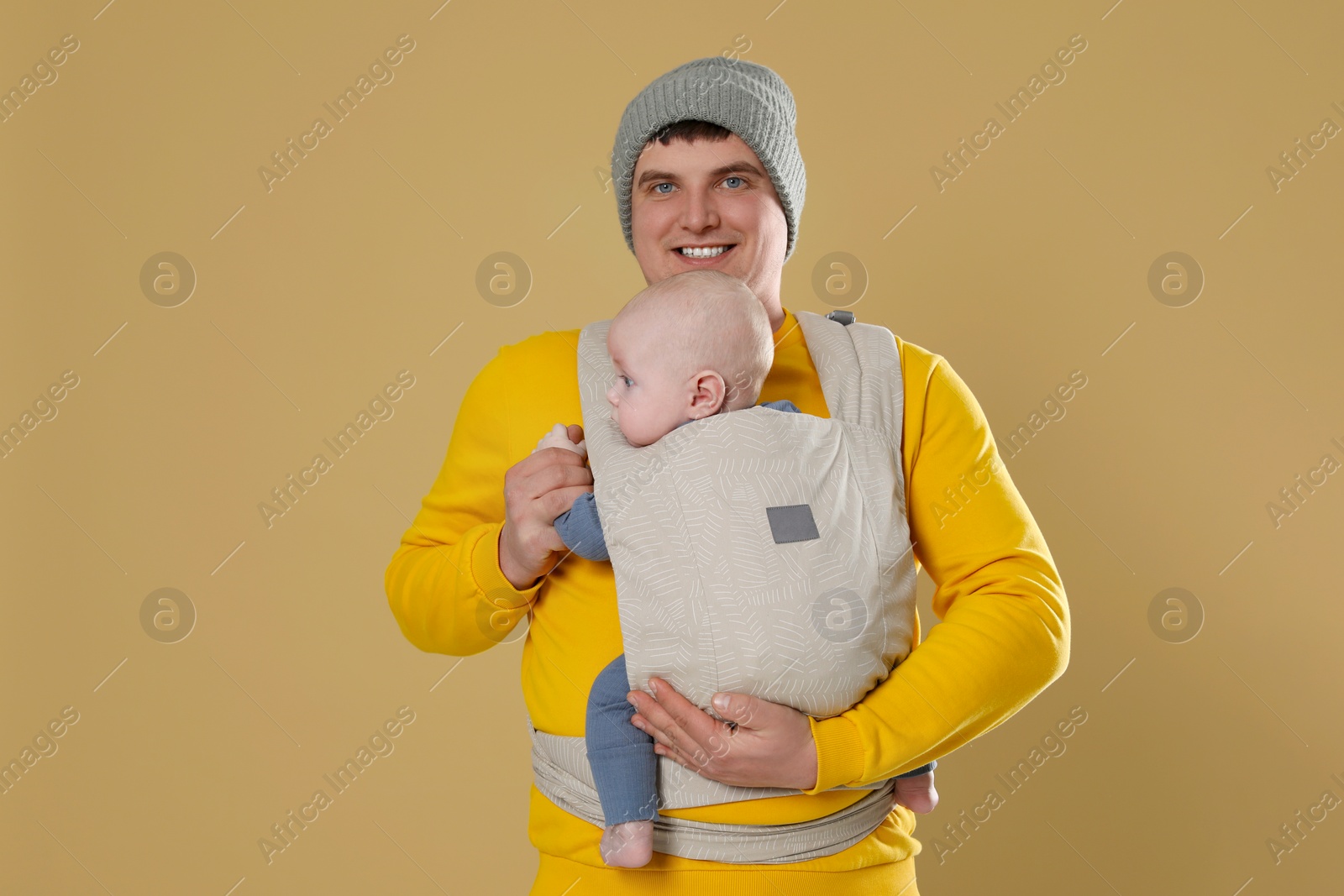 Photo of Father holding his child in sling (baby carrier) on beige background