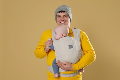 Photo of Father holding his child in sling (baby carrier) on beige background