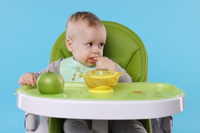 Photo of Cute little baby eating healthy food in high chair on light blue background