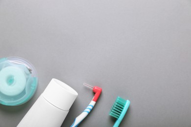 Container with dental floss and different teeth care products on light grey background, flat lay. Space for text