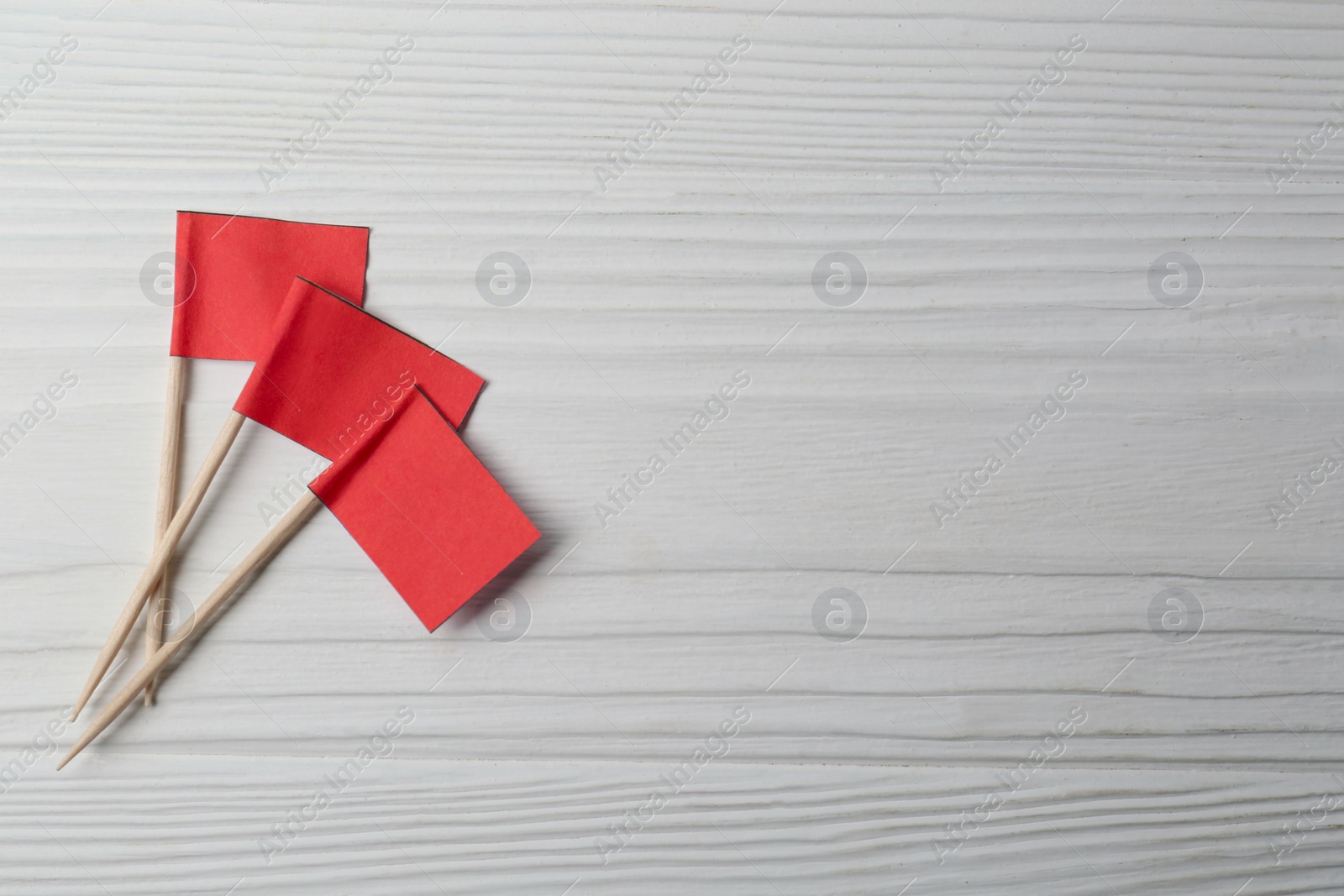 Photo of Small red paper flags on white wooden table, flat lay. Space for text