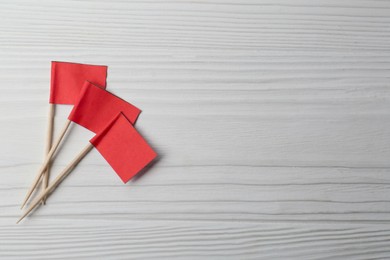 Small red paper flags on white wooden table, flat lay. Space for text