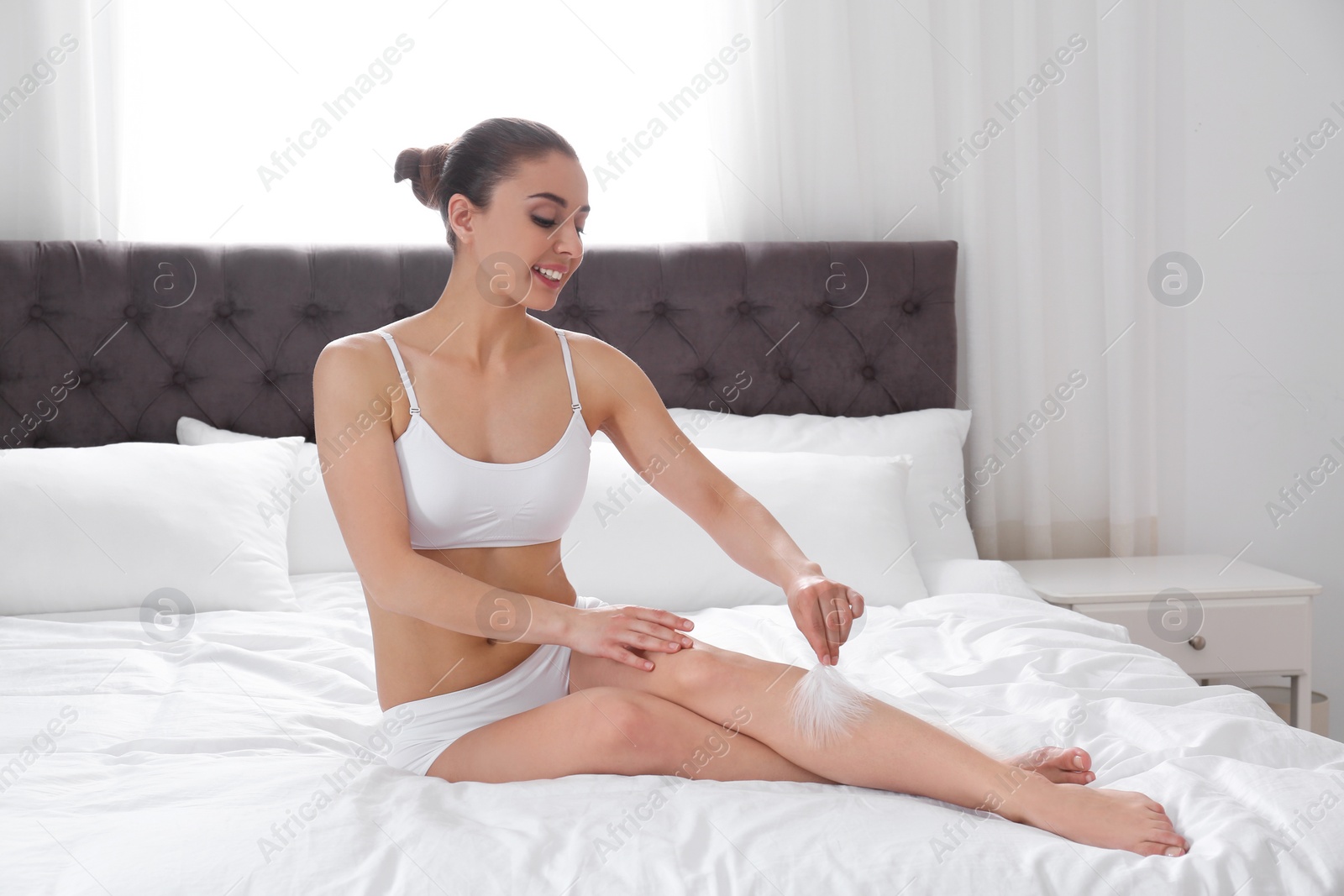 Photo of Woman touching leg with feather on bed at home. Epilation procedure