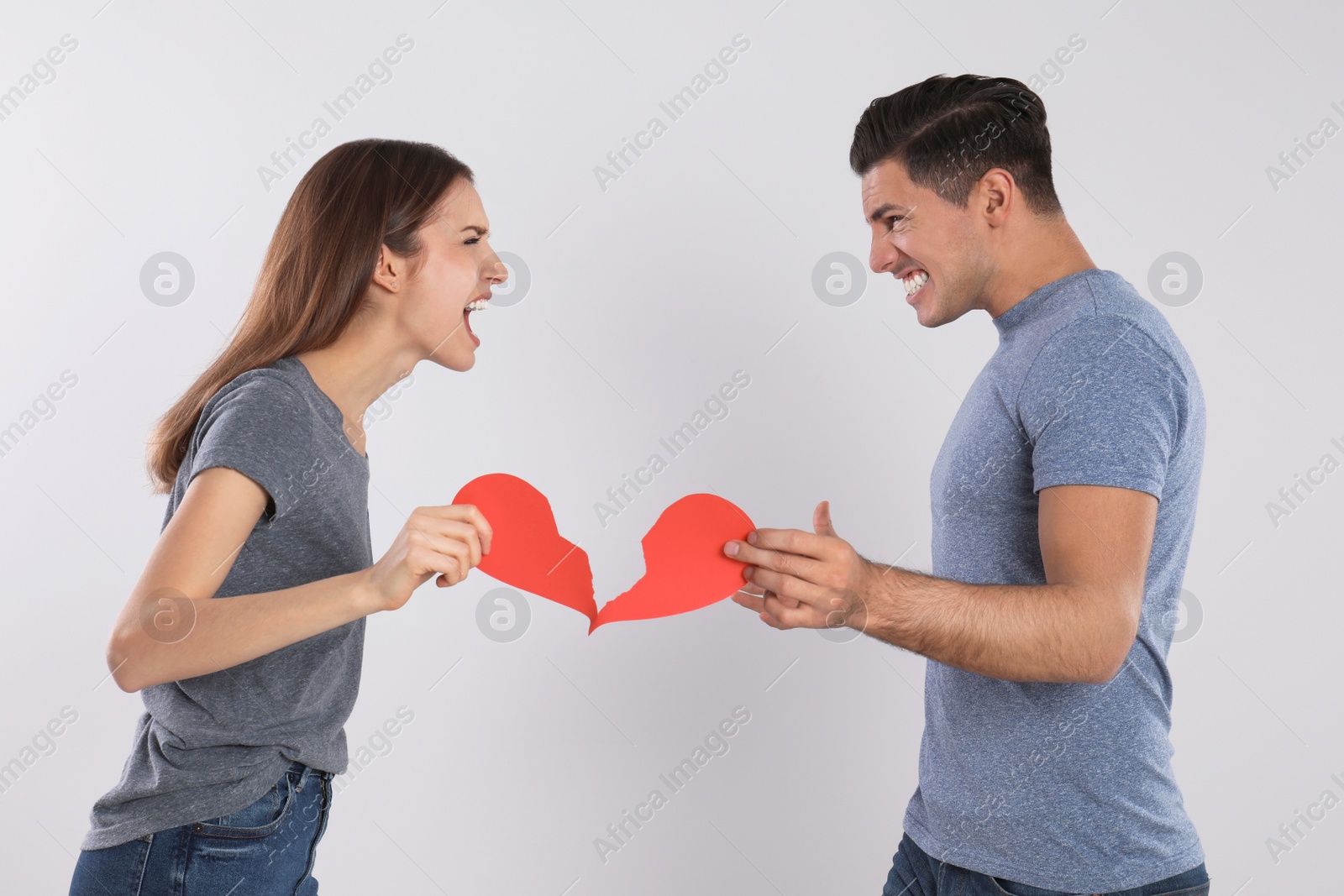 Photo of Couple with torn paper heart quarreling on light background. Relationship problems