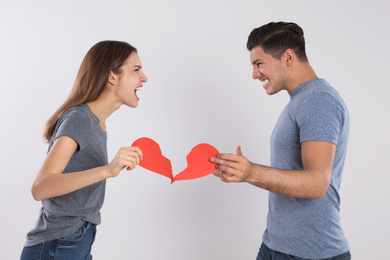 Couple with torn paper heart quarreling on light background. Relationship problems