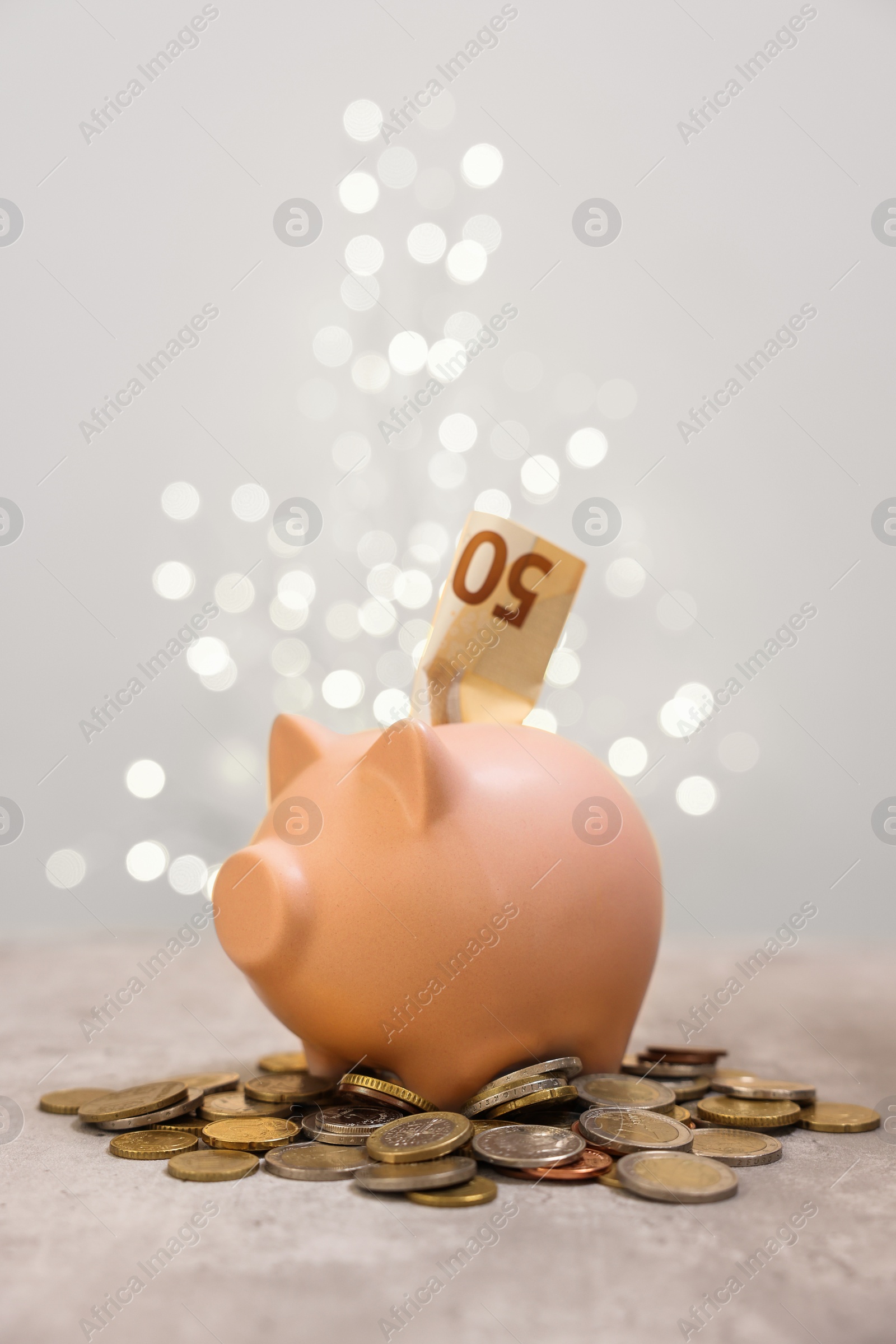 Photo of Piggy bank with euro banknote and coins on grey table against blurred lights, space for text