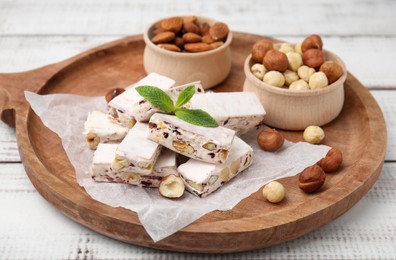 Pieces of delicious nougat and nuts on wooden board, closeup