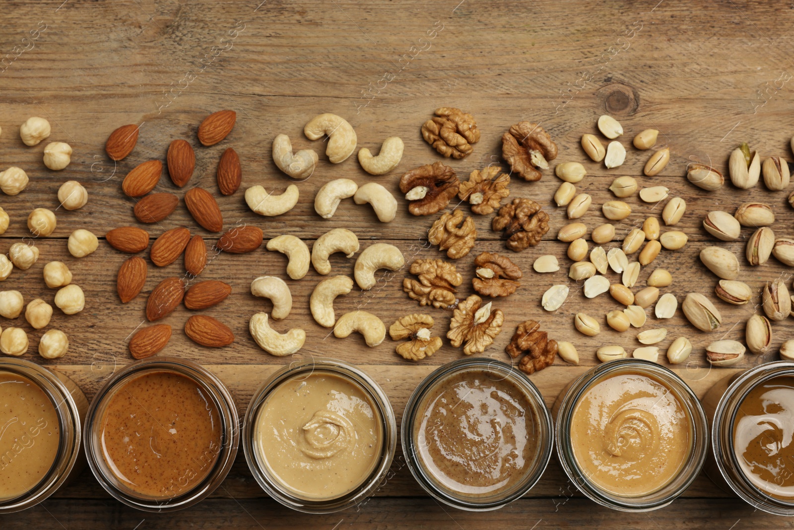 Photo of Nut butters in bowls and ingredients on wooden table, flat lay