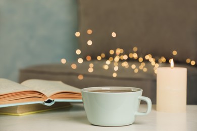 Photo of Cup of tasty freshly brewed tea, burning candle and open book on table