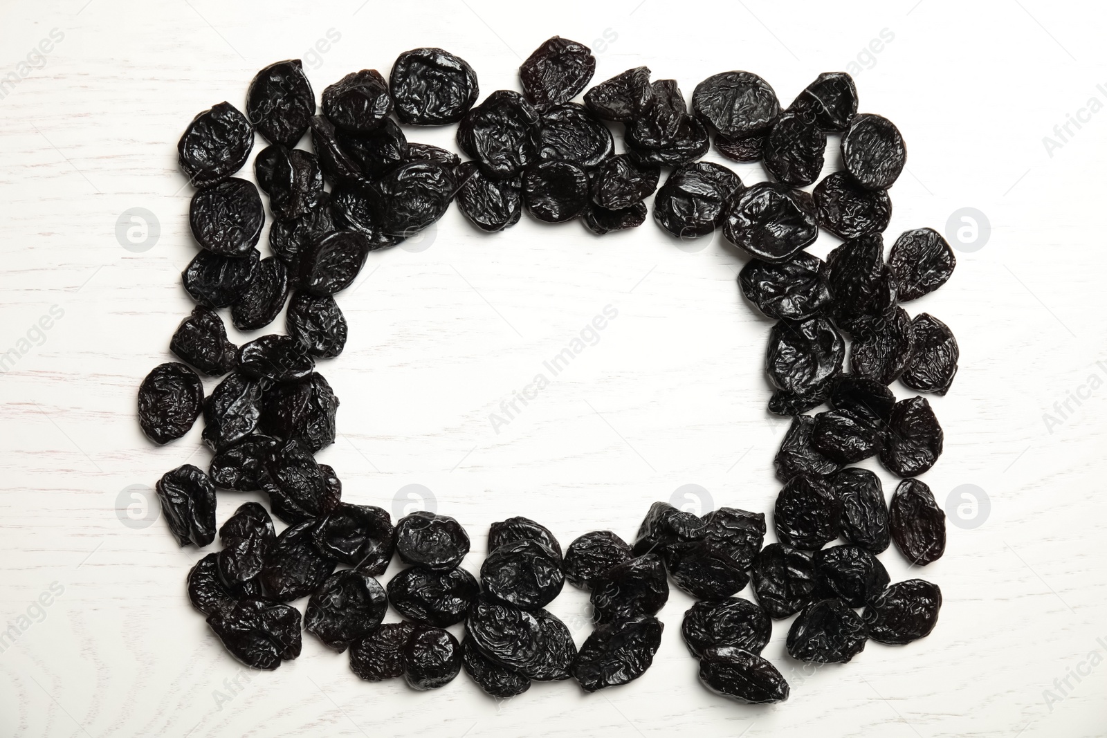 Photo of Frame of sweet dried plums on wooden background, top view with space for text. Healthy fruit