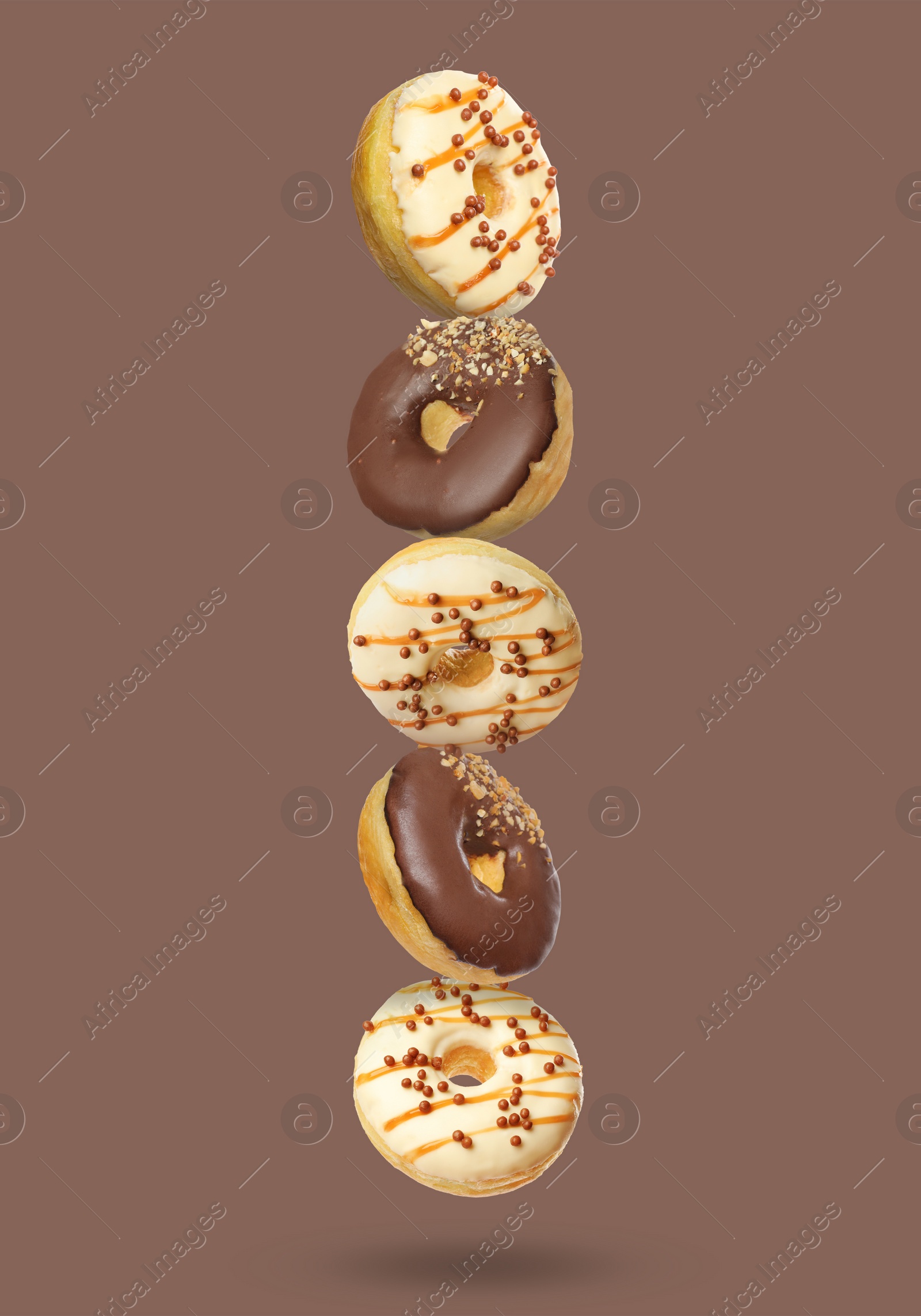 Image of Different tasty donuts falling on pastel brown background