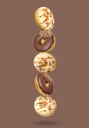 Image of Different tasty donuts falling on pastel brown background