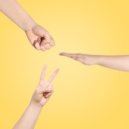 People playing rock, paper and scissors on yellow background, top view