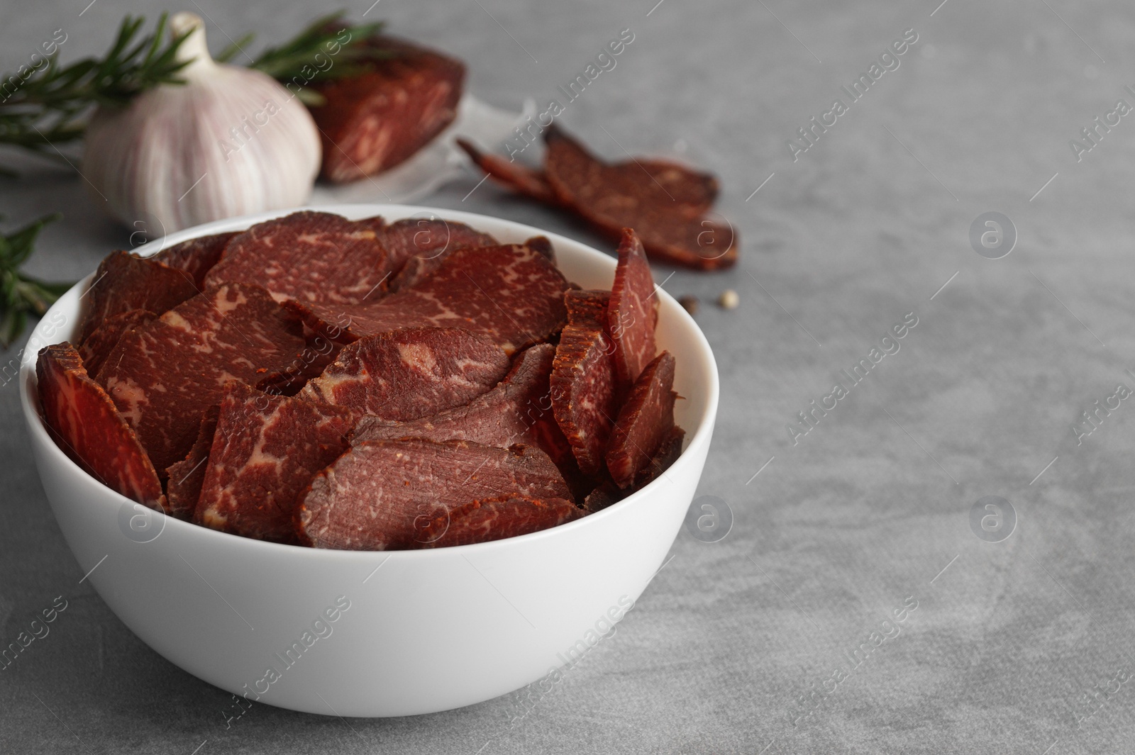 Photo of Delicious beef jerky in bowl on light gray table, space for text
