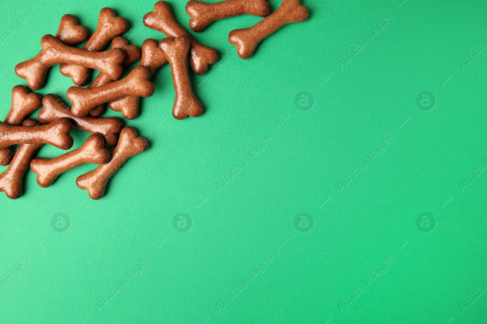 Photo of Bone shaped dog cookies on green background, flat lay. Space for text