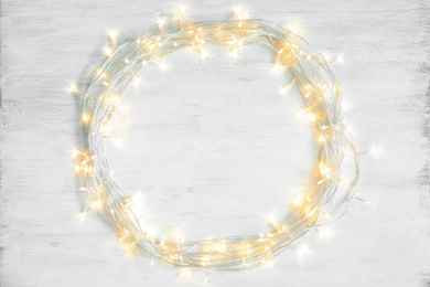 Glowing Christmas lights on wooden background, top view