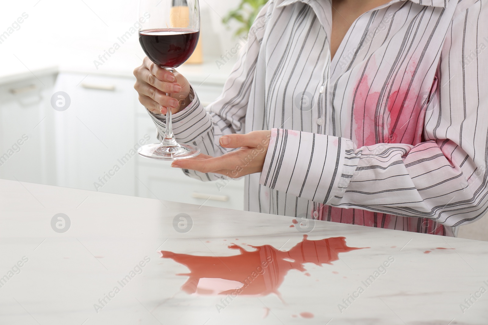 Photo of Woman with spilled wine over her shirt and marble table in kitchen, closeup