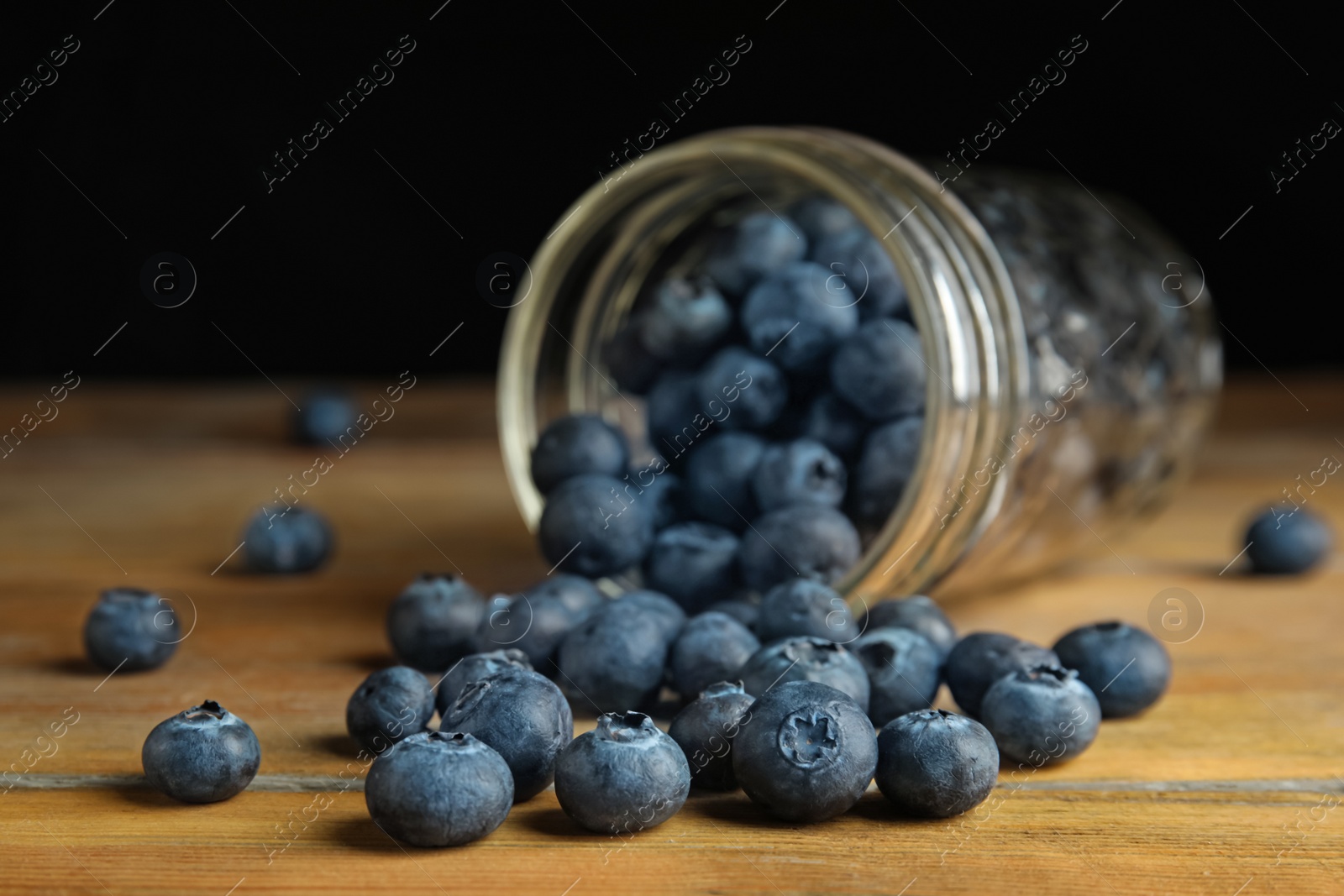 Photo of Overturned glass jar of ripe blueberries on wooden table, closeup