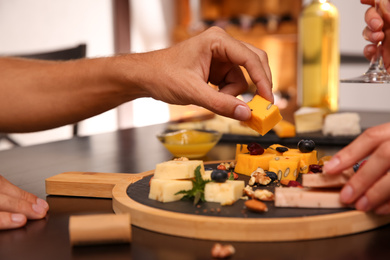 Photo of Couple with different types of delicious cheeses at table indoors, closeup