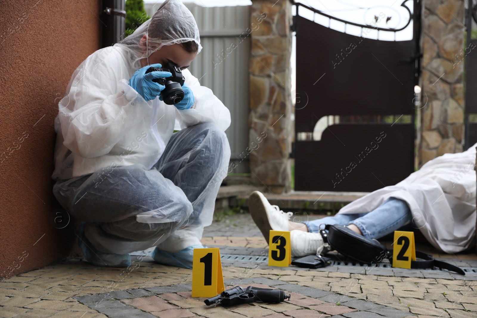Photo of Criminologist taking photo of evidence at crime scene with dead body near house