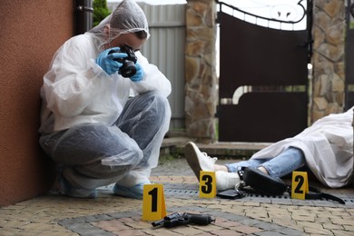 Photo of Criminologist taking photo of evidence at crime scene with dead body near house