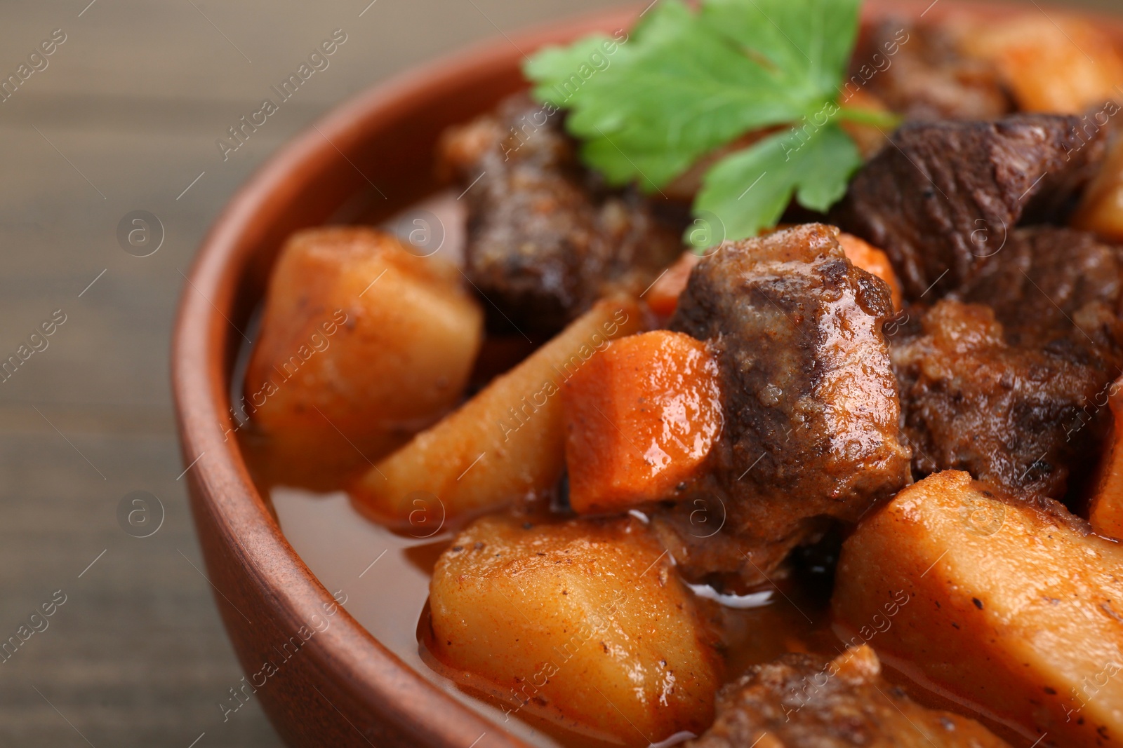 Photo of Delicious beef stew with carrots, parsley and potatoes on wooden table, closeup