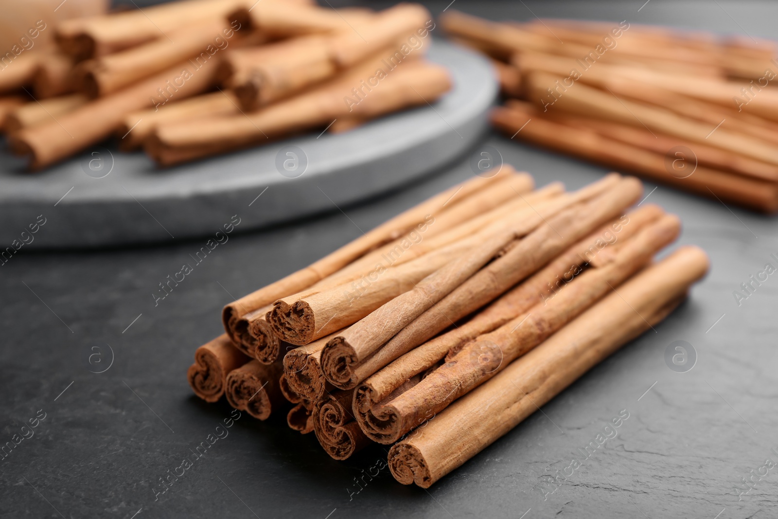 Photo of Pile of aromatic cinnamon sticks on black table, closeup