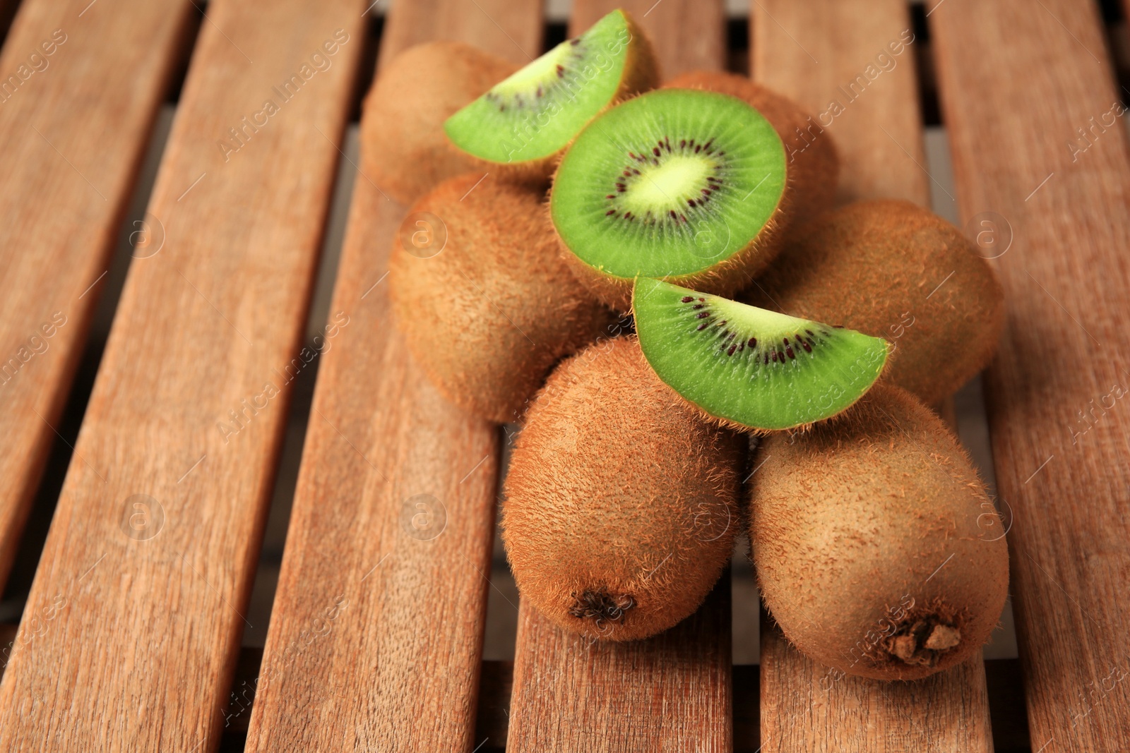 Photo of Whole and cut kiwis on wooden table, closeup. Space for text