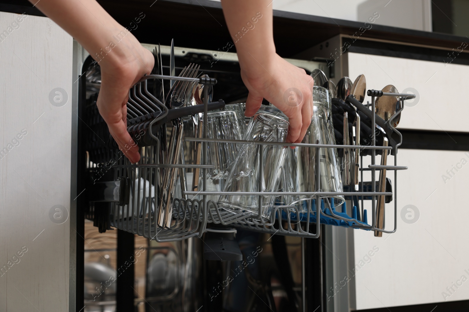 Photo of Woman loading dishwasher with glass and cutlery indoors, closeup