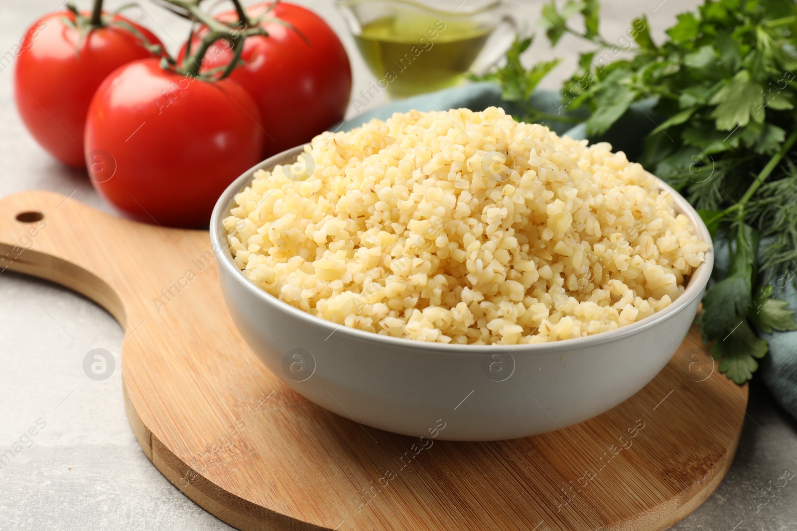 Photo of Delicious bulgur in bowl, greens and tomatoes on table, closeup