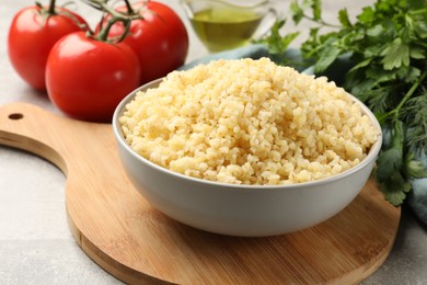 Delicious bulgur in bowl, greens and tomatoes on table, closeup