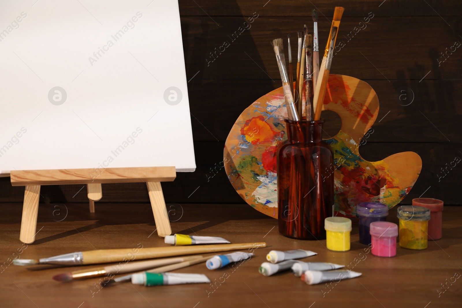 Photo of Easel with canvas and art supplies on wooden table