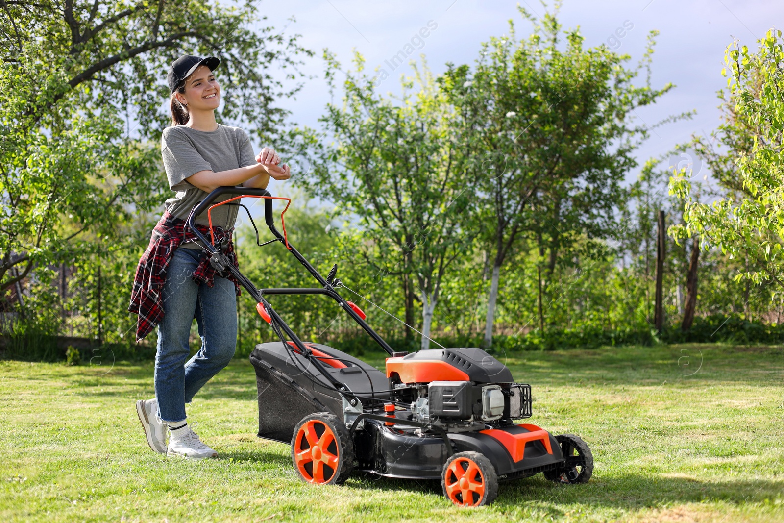 Photo of Smiling woman cutting green grass with lawn mower in garden