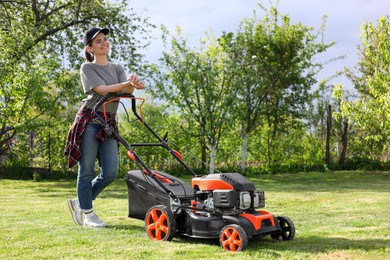 Photo of Smiling woman cutting green grass with lawn mower in garden