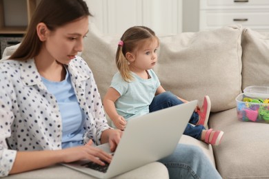 Woman with laptop working remotely at home. Mother and daughter on sofa in living room