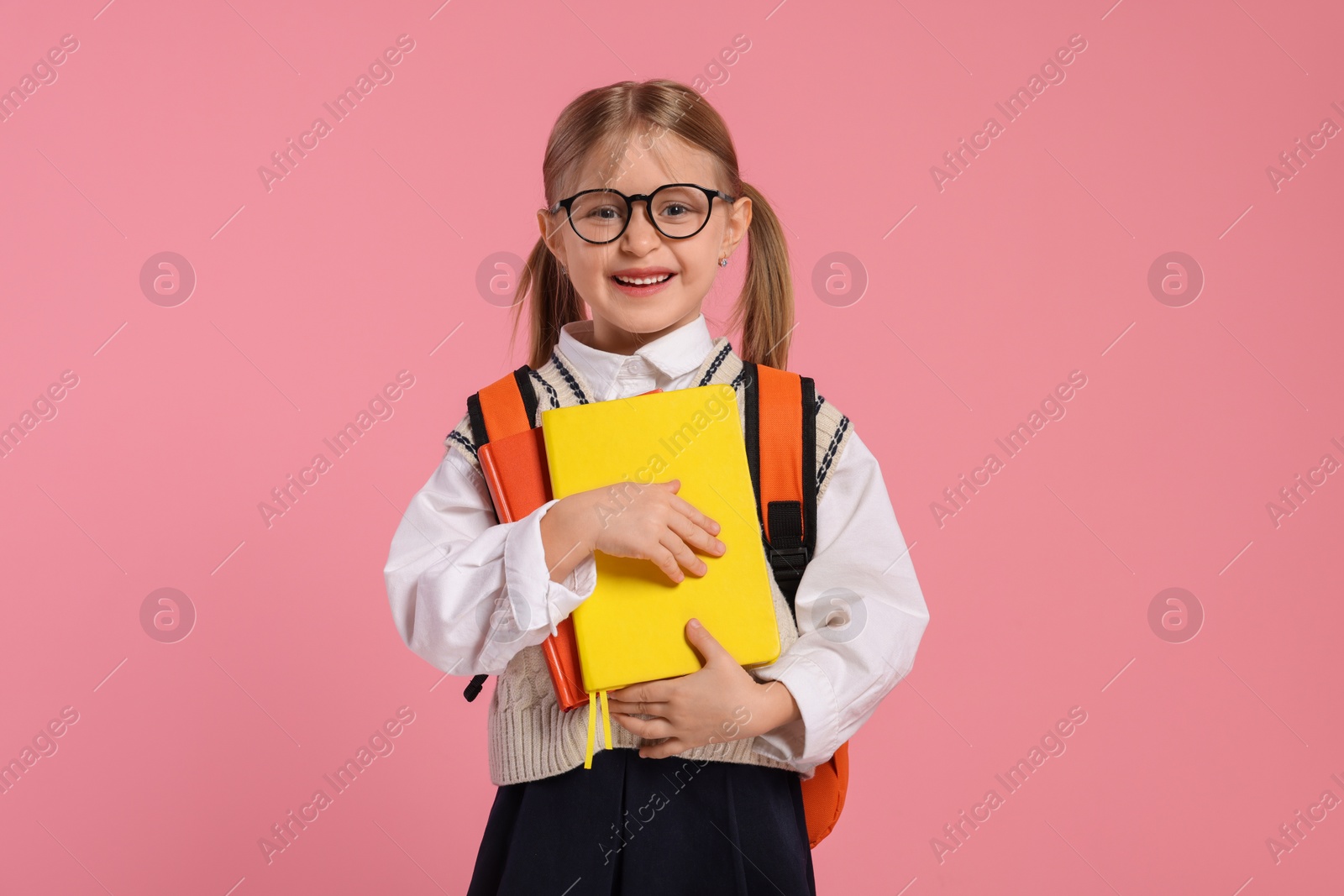 Photo of Happy schoolgirl in glasses with backpack and books on pink background