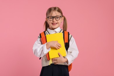 Happy schoolgirl in glasses with backpack and books on pink background