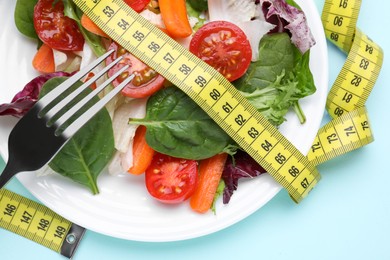 Photo of Measuring tape, vegetable salad and fork on light blue background, flat lay. Weight loss concept
