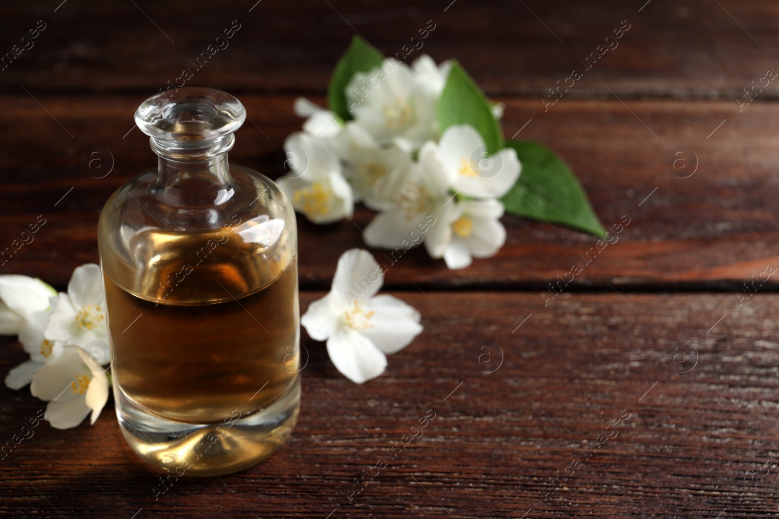 Photo of Essential oil and jasmine flowers on wooden table. Space for text