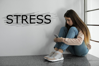 Depressed young girl sitting on floor indoors and word STRESS