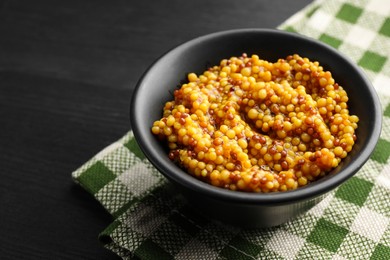 Photo of Whole grain mustard in bowl on black wooden table, closeup. Space for text