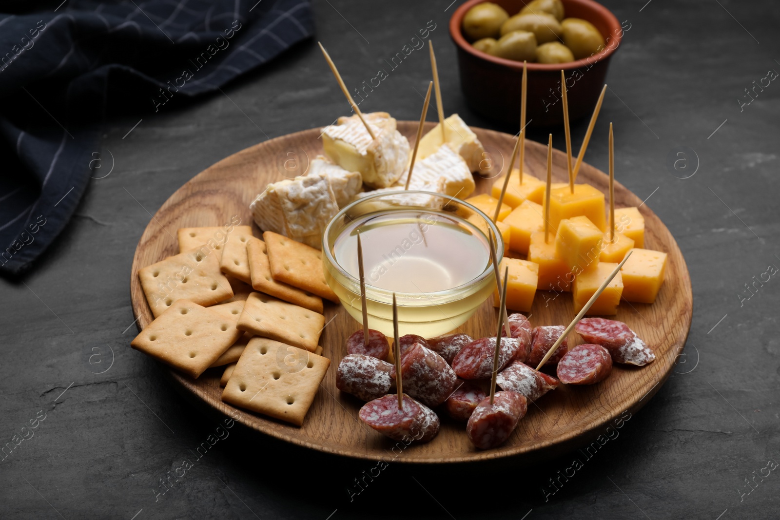 Photo of Toothpick appetizers. Pieces of sausage, crackers and honey on black table