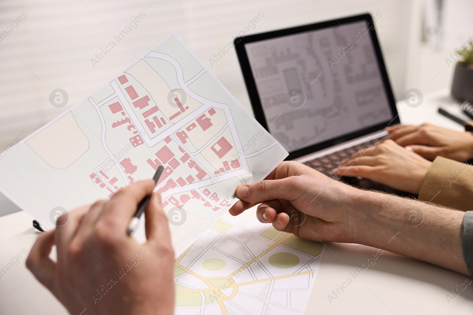 Photo of Cartographers working with cadastral maps at white table in office, closeup