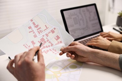 Photo of Cartographers working with cadastral maps at white table in office, closeup