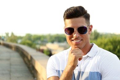Photo of Handsome man wearing stylish sunglasses on city street. Space for text