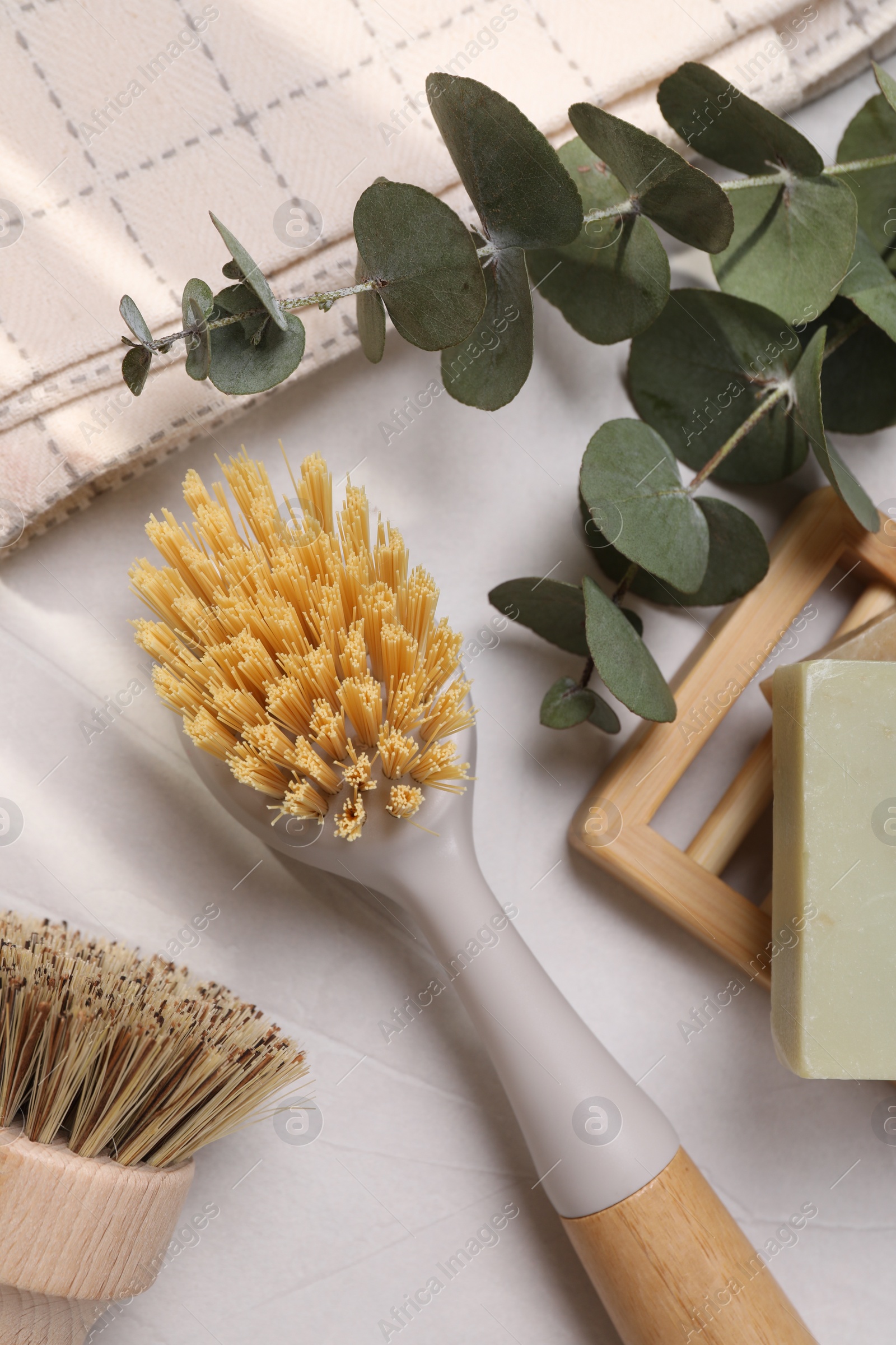 Photo of Cleaning brushes, soap bar and eucalyptus leaves on white table, flat lay