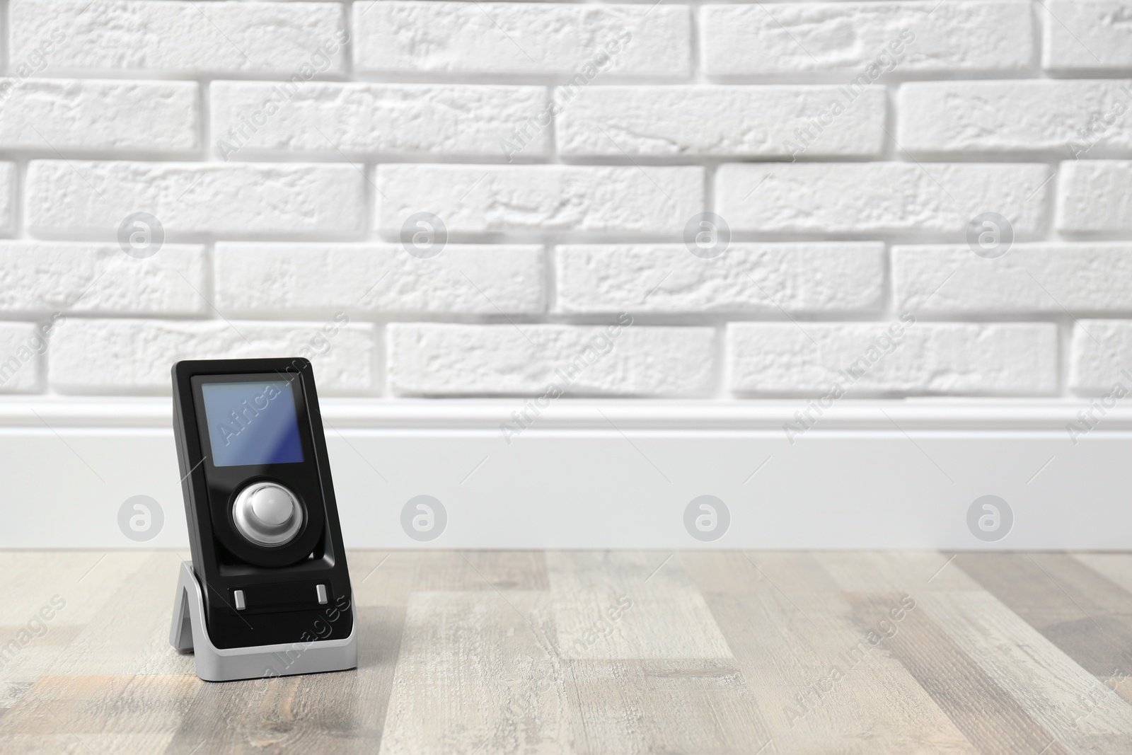 Photo of Modern audio speaker remote on floor near white brick wall. Space for text